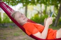 Young woman reading on electronic tablet reader relaxing in hammock under palm trees Royalty Free Stock Photo