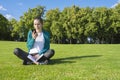 A young woman reading a message on the phone in the park on the grass. Education and knowledge