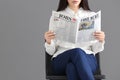 Young woman reading newspaper against grey background Royalty Free Stock Photo