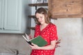 Young woman reading recipe book at home kitchen, thinking what to cook for dinner Royalty Free Stock Photo