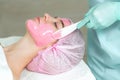 Young woman receiving pink facial mask.