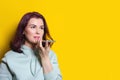 Young woman is recording an audio message on her smartphone. Horizontal studio shot on yellow background