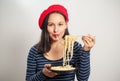 Young woman in a red beret eating spaghetti. On white