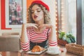 Young woman in red beret sitting in cafe, drinking coffee and eating french croissant Royalty Free Stock Photo