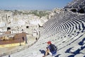 A woman in red cap and blue t-shirt sitting on steps in ancient amphitheater in Side, Turkey