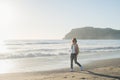 Young woman in red checkered shirt, jeans, white sneakers walking along beach and the stormy ocean on sunny winter day Royalty Free Stock Photo