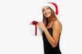 Happy young woman in red Christmas hat and black dress holding a gift box on a white background, Concept of Christmas, holiday Royalty Free Stock Photo