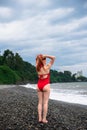 A young woman in a red closed swimsuit. Stormy Black sea with waves, Heavy thunderstorms on the horizon. Sunset. Rocky beach. Royalty Free Stock Photo