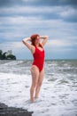 A young woman in a red closed swimsuit. Stormy sea with big waves, Heavy thunderstorms on the horizon. Sunset. Rocky beach. Royalty Free Stock Photo