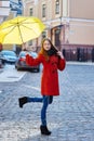 Young woman in a red coat with yellow umbrella walks through the city Royalty Free Stock Photo