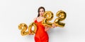 Young woman in red cocktail dress with bright make-up celebrating New Year 2022 and holding golden balloons 2022 in Royalty Free Stock Photo