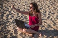 Young woman in red dress with computer and smartphone on the beach. Freelance and downshifting concept. Royalty Free Stock Photo