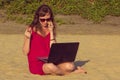 Young woman in red dress with computer and smartphone on the beach. Freelance and downshifting concept. Royalty Free Stock Photo