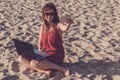 Young woman in red dress with computer and smartphone on the beach. Freelance and downshifting concept. Royalty Free Stock Photo