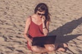 Young woman in red dress with computer and smartphone on the beach. Freelance and downshifting concept. Royalty Free Stock Photo