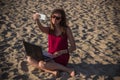 Young woman in red dress with computer and smartphone on the beach. Freelance and downshifting concept.