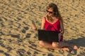 Young woman in red dress with computer and smartphone on the beach. Freelance and downshifting concept.