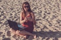 Young woman in red dress with computer and smartphone on the beach. Freelance and downshifting concept.