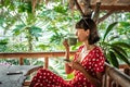 Young Woman In Red Dress Drinking A Coffee In A Tropical Restaurant On Bali Island. Travel, Jungle, Rainforest Of Indonesia.