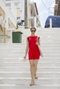 Young woman in red dress, holding white hat in hand, going downstairs