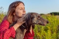 A young woman in a red dress hugs a greyhound dog outdoors and looks into the distance Royalty Free Stock Photo