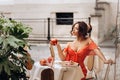 Young woman in red dress sits at table with cups, teapot, cake, pomegranates