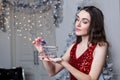 A young woman in a red dress smiles holding a small shopping cart in her hand on the background of a Christmas tree Royalty Free Stock Photo