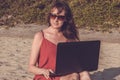 Young woman in red dress is working on laptop on the beach. Free