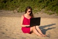 Young woman in red dress is working on laptop on the beach. Free Royalty Free Stock Photo