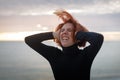 Young woman with red hair clutching at her head writhing in pain on the background of sea and sunset