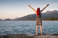 Young woman with red hair is embracing the wonderful nature near the ocean with mountains and forest