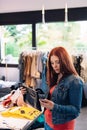 young red-haired woman looking at price tags of clothes to buy, in a fashion shop. shopping concept. leisure concept. Royalty Free Stock Photo