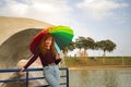 Young woman, red hair, freckles, with a rainbow umbrella, under a waterfall, in an outdoor park. Concept color, happiness, well-