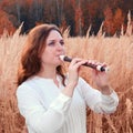 A young woman with red hair plays a flute in an autumn grass