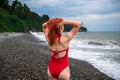 A young woman with red hair in a red closed swimsuit. Stormy sea with big waves, Heavy thunderstorms on the horizon. Sunset. Rocky Royalty Free Stock Photo