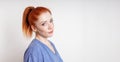 young woman with red hair tied in ponytail tilts her head smiling