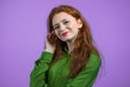 Young woman with red hairstyle looking to camera, flirting. Beautiful model girl on violet studio background.