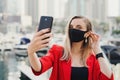 Young woman in red jacket wearing protective face mask of black color taking a selfie photo Royalty Free Stock Photo