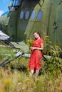 Young woman in a red pin up dress with a bunch of yellow wildflowers stands by an airplane Royalty Free Stock Photo