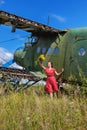 Young woman in a red pin up dress waving a bunch of flowers to someone at an abandoned airplane Royalty Free Stock Photo