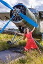 Young woman in a red pin up style dress stands by an abandoned small propeller plane Royalty Free Stock Photo