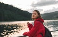 Young woman in a red raincoat looking at the camera, smiling, enjoying staying in the woods near the lake. Cute attractive girl Royalty Free Stock Photo