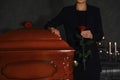 Young woman with red rose near casket in funeral home,