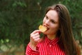 Young woman in red shirt eating potato chips with blurred trees on the background. Royalty Free Stock Photo