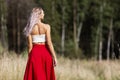 Young woman in a red skirt in the field. Back view. Power of nature