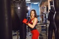 Young woman in red sports clothes and boxing gloves, trains with a boxing pear in a dark gym Royalty Free Stock Photo