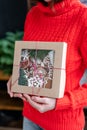 Young woman in red sweater holding in his hand Christmas gift, homemade gingerbread. Biscuits in festive packaging. Royalty Free Stock Photo