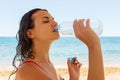 Young woman in a red swimsuit, drinking sparkling water from a transparent bottle on the beach Royalty Free Stock Photo