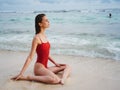 A young woman in a red swimsuit sits on the sand with a beautiful sun tan and looks out at the ocean in the tropics on Royalty Free Stock Photo