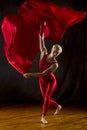 Young woman in red unitard swirling red fabric in studio. Royalty Free Stock Photo